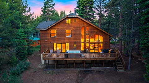 Twilight mountain lodge with a spacious deck, private hot tub, and warm forest-side glow.