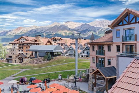 A picturesque mountain village with traditional architecture, a ski lift, and a stunning mountain backdrop under a cloudy sky.