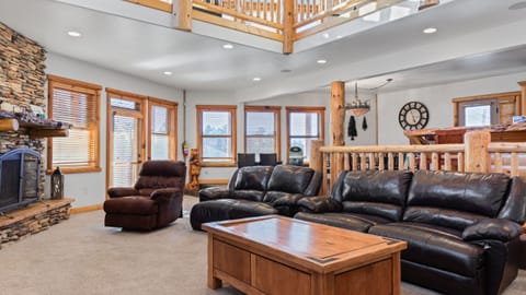 Spacious mountain-style living room with cozy seating, rustic wood accents, and a stone fireplace centerpiece.
