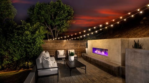Private backyard with outdoor lounge, fireplace, and string lights for evening relaxation.