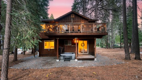 Back exterior view of the cabin, featuring a hot tub and a forest backdrop.
