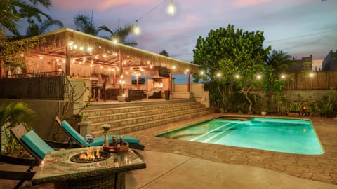 Tropical backyard oasis with a glowing pool, fire pit, tiki-style cabana, and dreamy sunset skies.