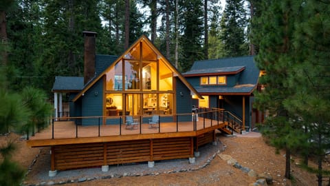 Warm, glowing cabin surrounded by towering pines with a wraparound deck made for mountain living.