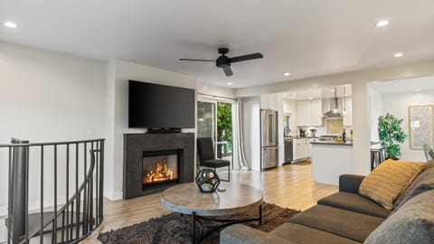 Cozy living room with fireplace, TV, ceiling fan, and sofa.