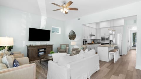 Open concept living room with a large sofa, area rug, mounted television, and ceiling fan.