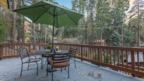 Open deck space with an umbrella, chairs, and a table, overlooking a wooded area.