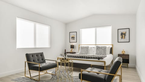 The primary bedroom features a king bed, gold accent chairs, and a small table set.