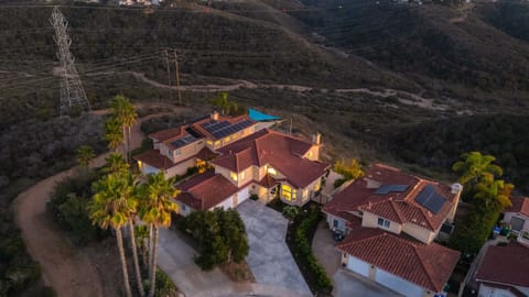 Aerial view of the large Mediterranean-style home and surrounding hilly landscape at sunset/dusk.