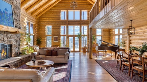Grand, open-concept log cabin interior with high ceilings, large windows, and a wooden floor.