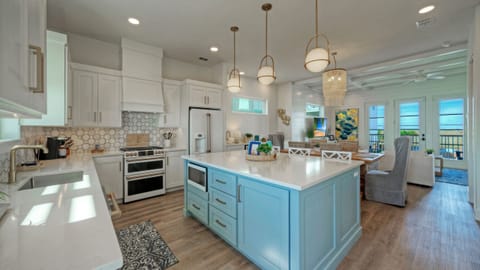 Open-concept kitchen with light blue island, white cabinetry, and hanging pendant lights.