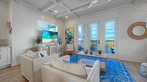 Bright living room with white sofas, a ceiling fan, and a TV.