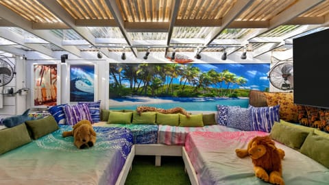 Covered lounge with daybeds, TV, and tropical décor for relaxed hangouts.