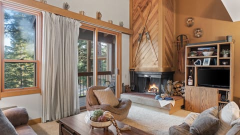Cozy living room with a roaring fireplace, rustic wood accents, and forest views from the sliding doors.
