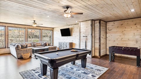 Lower-level lounge area with full-sized pool table in a spacious wood-paneled room.