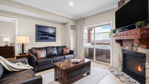 Warm and inviting living room with a stone fireplace, leather seating, and sliding doors leading to a private balcony with mountain views.
