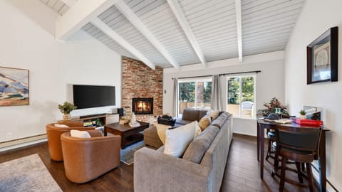 Open-concept living room featuring vaulted beamed ceilings, a stone fireplace, and leather armchairs.