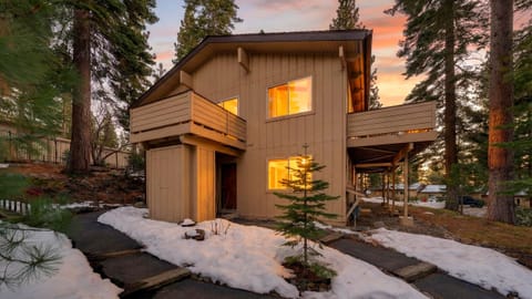 Dusk exterior of the multi-level mountain home with warm light glowing from the windows and snow on the ground.