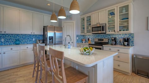 Bright kitchen featuring white cabinetry, a large island with seating, and blue tile backsplash.