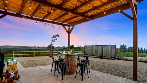 Covered outdoor patio with a dining table, chairs, and barrel accents at sunset. (Shimla Syrah)