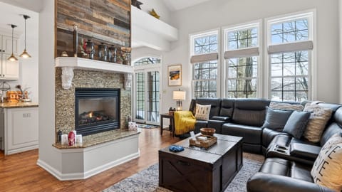 Spacious living room with vaulted ceilings, floor-to-ceiling windows, and a cozy stone fireplace.