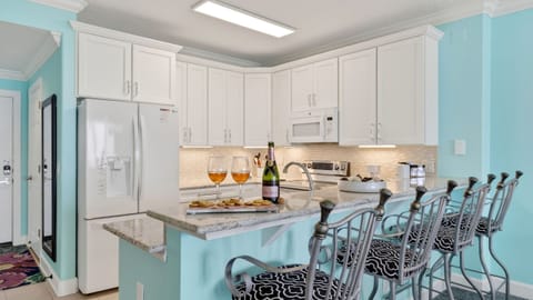 Bright coastal kitchen with bar seating—perfect for breakfast, snacks, and sunset happy hour at home.