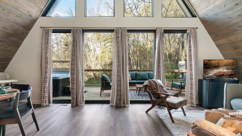 Vaulted A-frame living with wall-to-wall windows and seamless deck access—your private woodland view, all day long.