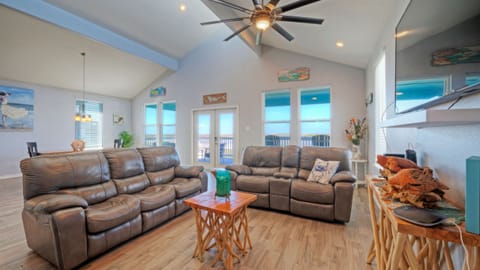 Bright, coastal living room with vaulted ceilings, comfy recliners, and bay-view balcony access.