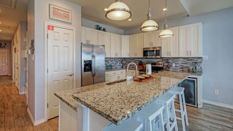 Spacious, fully stocked kitchen with granite island seating, stainless steel appliances, and bright pendant lighting.