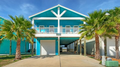 Bright coastal stilt home with palm-lined driveway and breezy balcony.