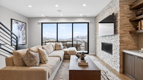 Wall-to-wall windows, a sleek fireplace, and a cozy sectional in the living room with mountain views right outside.