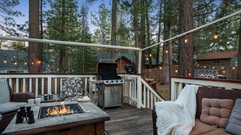 Spacious deck with a fire table, BBQ grill, and string lights for cozy evenings under the pines.