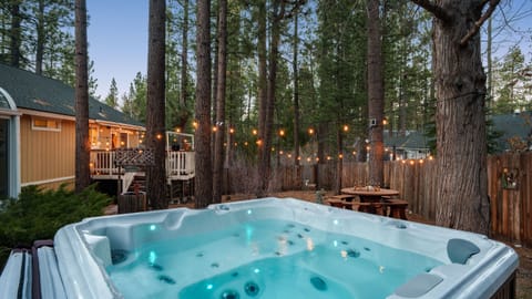 Hot tub nestled among the pines, complete with café lights and a peaceful mountain setting.