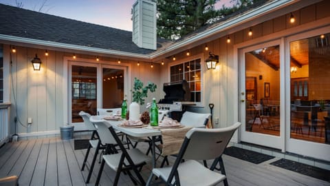 Inviting backyard deck with string lights, outdoor dining, and a grill—perfect for evening meals under the pines.