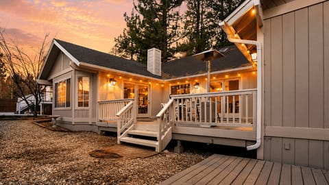 Inviting backyard deck with string lights, outdoor dining, and a grill—perfect for evening meals under the pines.