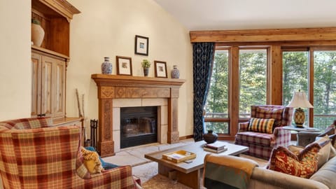 A warm, inviting living room with a fireplace and tall windows overlooking the trees.