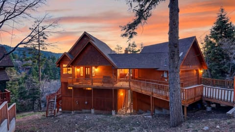 Warm, glowing mountain cabin surrounded by towering pines and sunset skies.