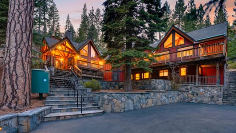Grand mountain lodge glowing with warm light, surrounded by towering pines and rustic stone pathways.