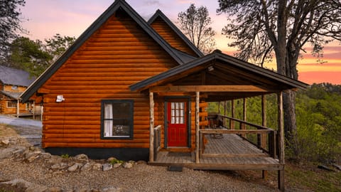 Covered cabin deck with a private hot tub, timber beams, and wide open views of the forested hills.