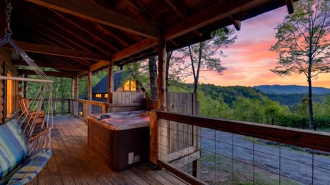 Covered deck with a private hot tub, hanging swing, and stunning Smoky Mountain sunset views.