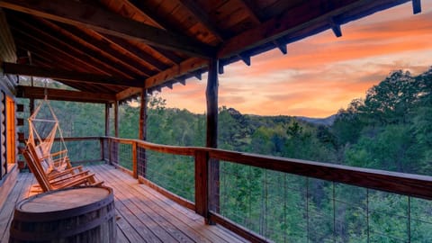 Expansive covered deck with rocking chairs, a hanging swing, and sweeping Smoky Mountain sunset views.