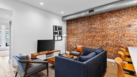 Modern open-concept living area featuring a plush dark sofa, wooden coffee table, and flat-screen TV setup.