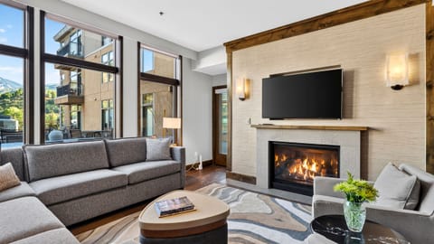 Cozy up by the fireplace in this bright living room, complete with plush seating, a large TV, and floor-to-ceiling windows.
