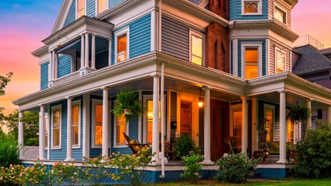Grand front exterior view highlighting detailed Victorian architecture, wrap-around porch, and mature trees.