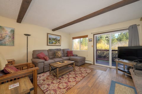 Unwind in your cozy living room with rustic beams overhead, plush seating, and peaceful forest views through sliding doors.