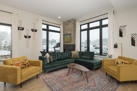 Relax in your stylish living room with plush velvet seating, stone fireplace, and panoramic windows framing winter mountain views.