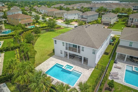 This aerial view showcases a spacious backyard with a sparkling pool, hot tub, and a cozy outdoor patio area. The home is nestled in a beautiful, serene neighborhood with plenty of greenery, offering a relaxing retreat for your next stay.