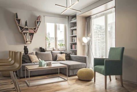 A modern living room with a gray sectional sofa, a green armchair, and a bookshelf near a large window.
