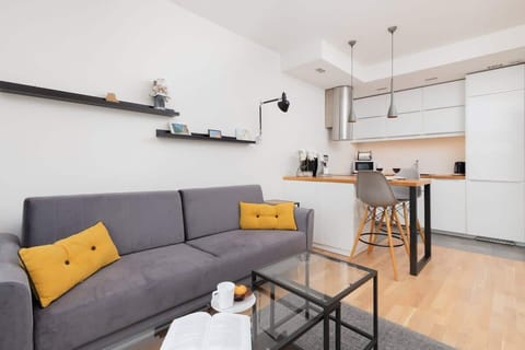 Modern living room with dining table – Cozy sofa with yellow pillows, smart TV, and a small dining space for two.