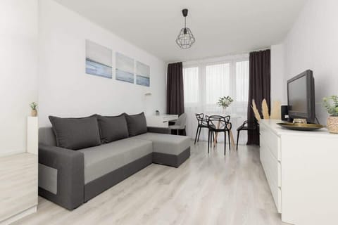 A bright living room with a gray sofa, a dining table, and modern decor in a minimalist white interior.
