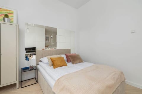 A bright bedroom with a double bed in beige bedding, a mirror above, and white walls for an airy look.
